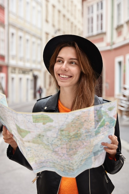 Happy holidaymaker searches right direction on map, explores new town with many sights