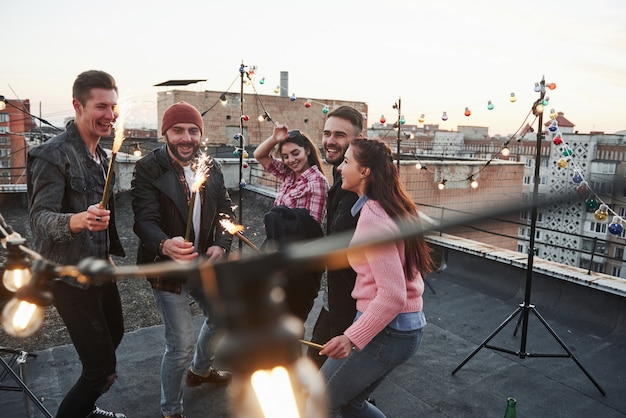 Free photo happy holidays. playing with sparklers on the rooftop. group of young beautiful friends