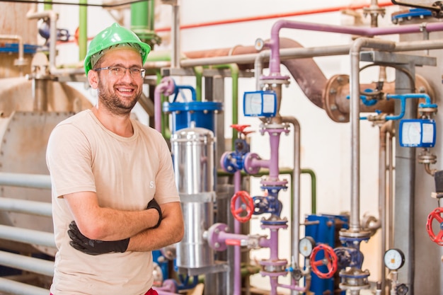 Happy Industry worker posing and smiling inside factory with bars and pipes around