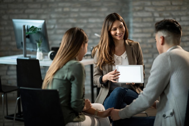 Happy insurance agent having a meeting with young couple and showing them potential investment possibilities on touchpad Copy space