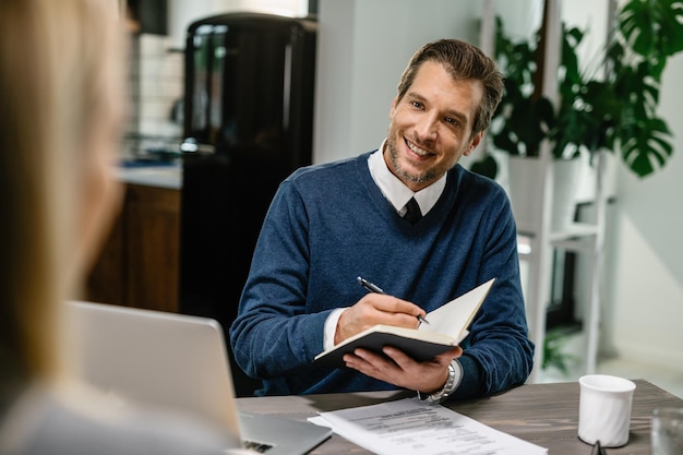 Happy insurance agent talking to a client and taking notes during the meeting