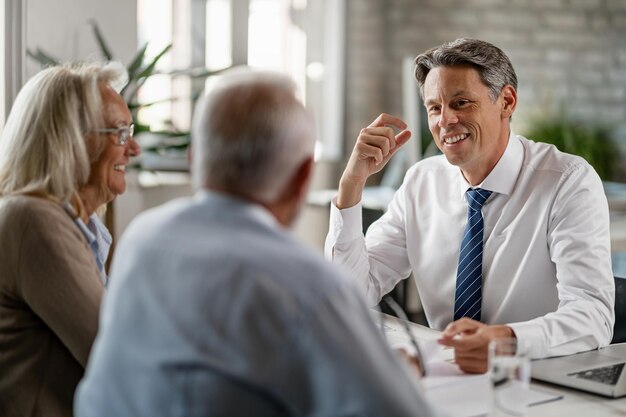 Счастливый страховой агент разговаривает со зрелой парой об их пенсионных планах во время встречи в офисе