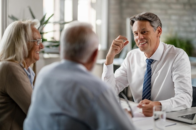 Happy insurance agent talking with mature couple about their retirement plans during the meeting in the office