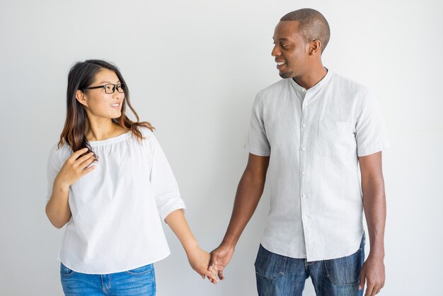 Happy interracial couple holding hands and looking at each other in studio.