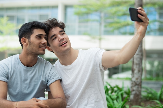 Free photo happy interracial gays posing for cute selfie in city