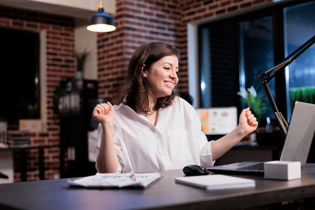 Happy joyful young adult businesswoman celebrating finishing startup project before deadline. Enthusiastic positive young adult entrepreneur being excited about new job while in office at night.