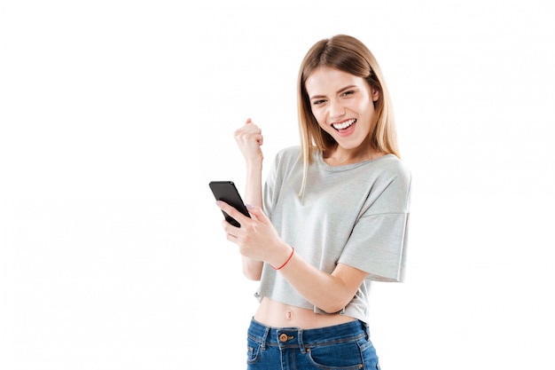 Happy joyful young woman holding mobile phone and celebrating a win