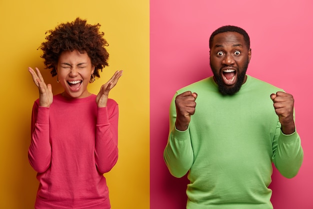 Happy joyous woman raises palms near face, emotional excited bearded Afro American man clenches fists and exclaims hooray, supports favorite football team. People, emotions, reaction concept