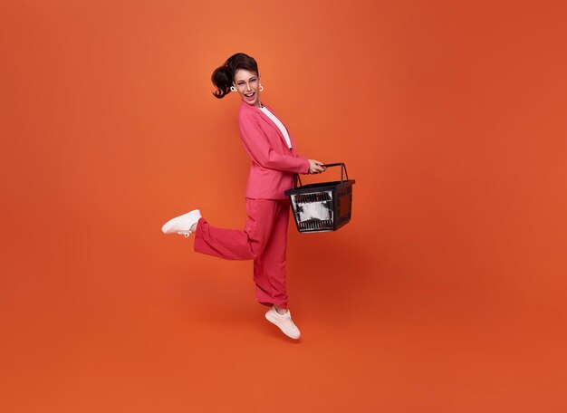 Happy jumping woman holding shopping basket isolated on orange studio background