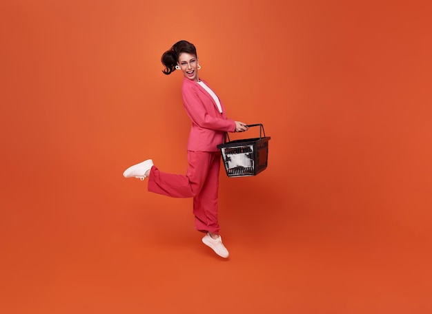 Happy jumping woman holding shopping basket isolated on orange studio background