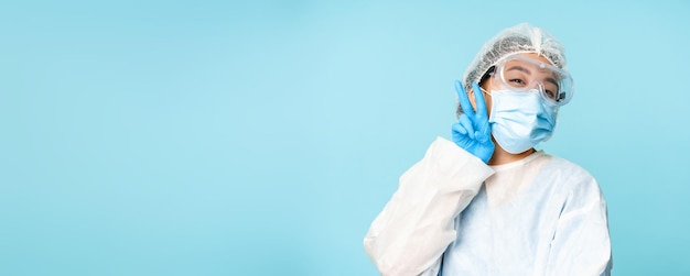 Happy kawaii asian female doctor nurse in personal protective equipment showing vsign peace gesture