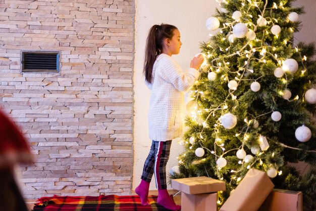 크리스마스 트리 위에 방에서 웃 고 행복 한 꼬마 소녀. 세련된 스웨터를 입고. 어린 시절. 크리스마스 때.