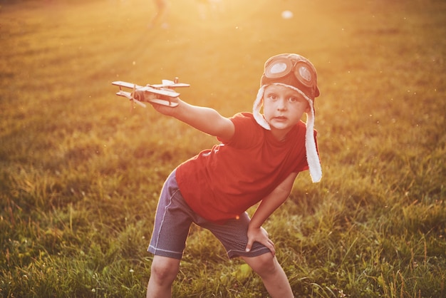 Счастливый малыш в пилотном шлеме играет с деревянным игрушечным самолетом и мечтает стать летающим