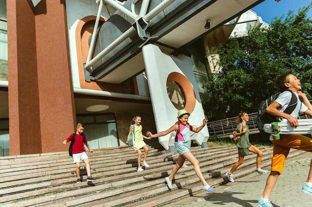 Foto gratuita bambini felici che giocano in strada della città nella soleggiata giornata estiva di fronte a un edificio moderno. gruppo di bambini o adolescenti felici divertendosi insieme. concetto di amicizia, infanzia, estate, vacanze.