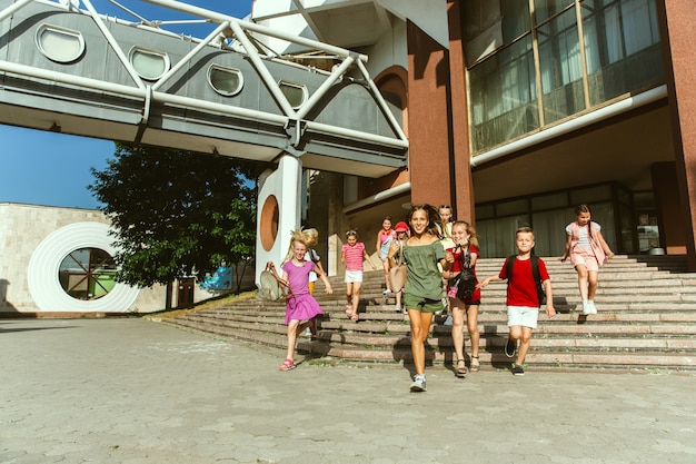 モダンな建物の前で晴れた夏の日に街の通りで遊んで幸せな子供たち。一緒に楽しんでいる幸せな子供やティーンエイジャーのグループ。友情、子供時代、夏、休日の概念。