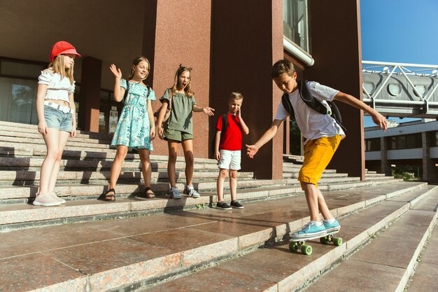 Счастливые дети, играющие на улице города в солнечный летний день перед современным зданием. Группа счастливых детей или подростков, весело проводящих время вместе. Понятие дружбы, детства, лета, праздников.