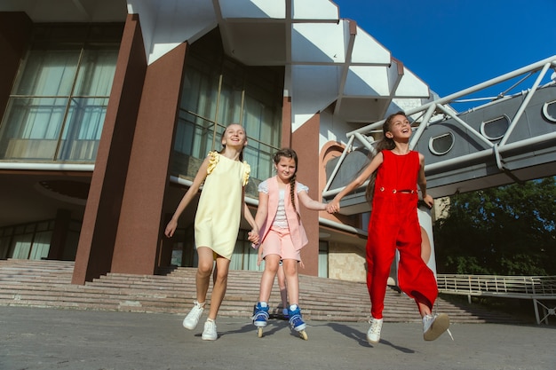 モダンな建物の前で晴れた夏の日に街の通りで遊んで幸せな子供たち。一緒に楽しんでいる幸せな子供やティーンエイジャーのグループ。友情、子供時代、夏、休日の概念。