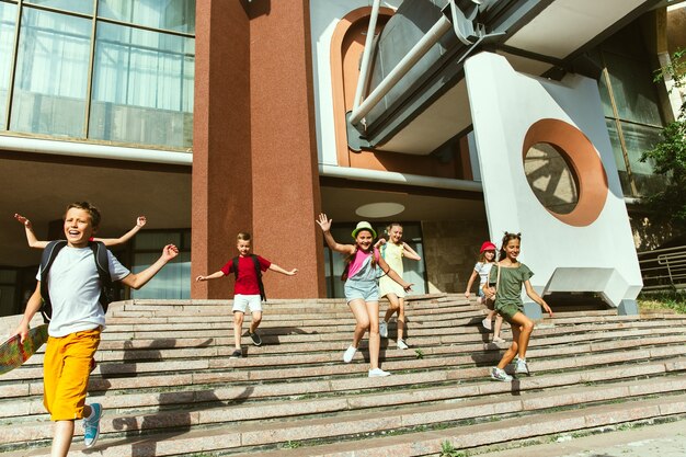 현대적인 건물 앞에서 화창한 여름 날에 도시의 거리에서 노는 행복한 아이들. 행복 한 어린이 또는 청소년이 함께 재미의 그룹입니다. 우정, 어린 시절, 여름, 휴일의 개념.