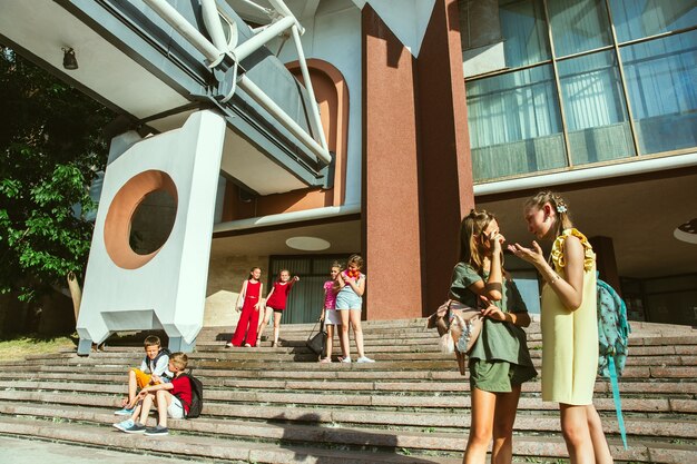 Happy kids playing at city's street in sunny summer's day in front of modern building. Group of happy childrens or teenagers having fun together. Concept of friendship, childhood, summer, holidays.