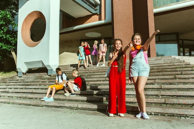 Happy kids playing at city's street in sunny summer's day in front of modern building. Group of happy childrens or teenagers having fun together. Concept of friendship, childhood, summer, holidays.