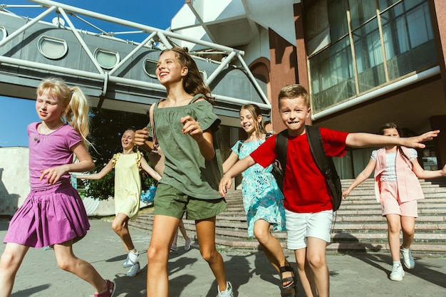 Happy kids playing at city's street in sunny summer's day in front of modern building. Group of happy childrens or teenagers having fun together