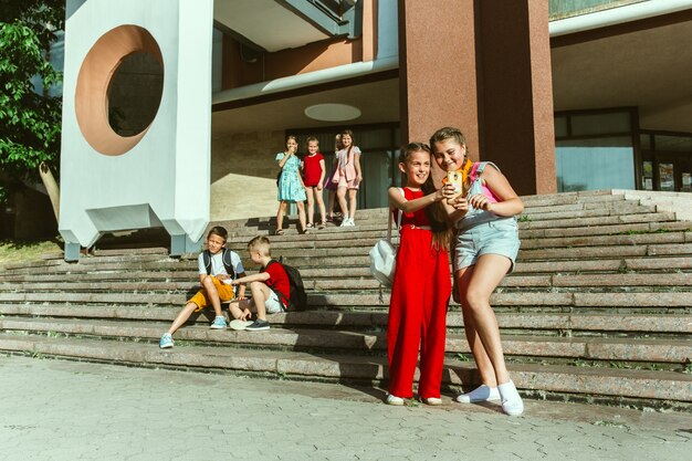 Happy kids playing at city's street in sunny summer's day in front of modern building. Group of happy childrens or teenagers having fun together