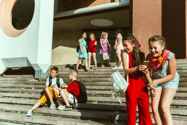 Foto gratuita bambini felici che giocano in strada della città nella soleggiata giornata estiva di fronte a un edificio moderno. gruppo di bambini felici o adolescenti che hanno divertimento insieme