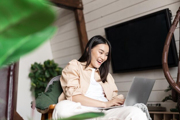 Happy korean girl celebrating looking excited at laptop reading good news on computer screen sitting...