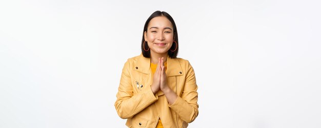 Happy korean woman looking hopeful asking for help favour begging standing with namaste gesture and smiling standing over white background