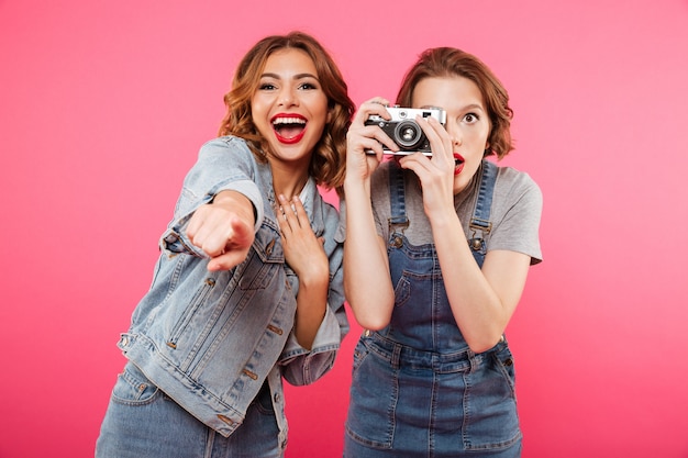 Happy ladies make photo by camera and pointing to you.