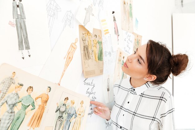 Happy lady fashion illustrator standing near a lot of illustrations