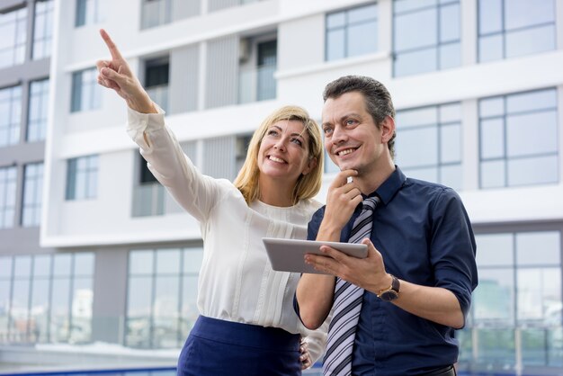 Happy lady pointing and showing male colleague something outdoors.