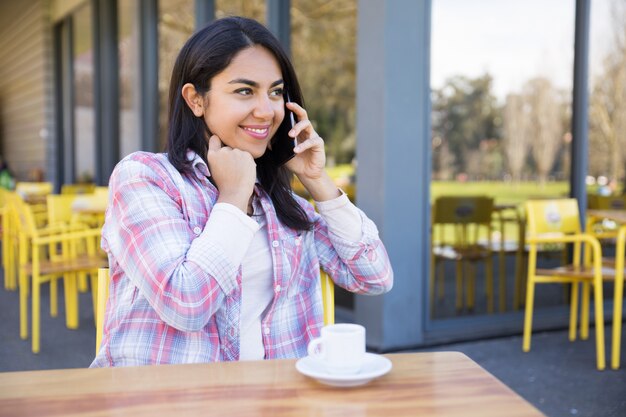 Счастливая леди разговаривает по телефону и пьет кофе в уличном кафе