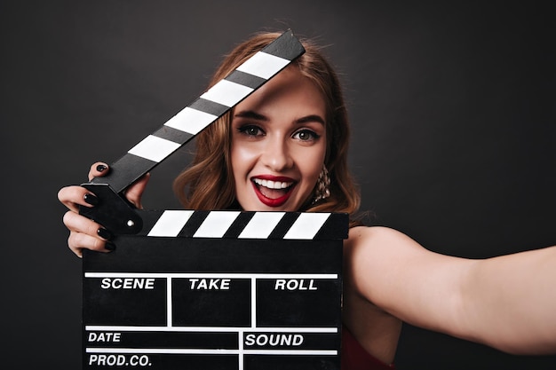 Free photo happy lady with beautiful makeup holding clapperboard on black background