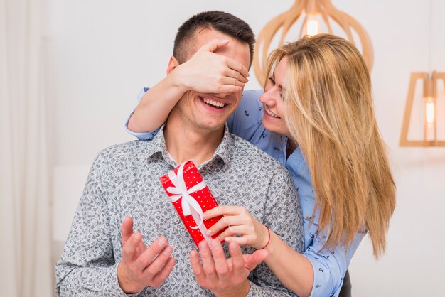 Happy lady with present closing eyes to smiling guy