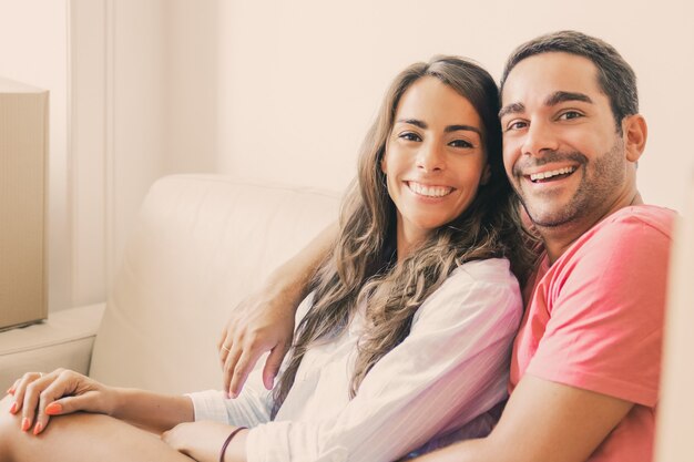 Happy Latin couple sitting on couch among carton boxes in new house