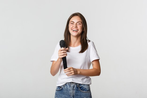 Happy laughing girl holding microphone and singing karaoke, white.