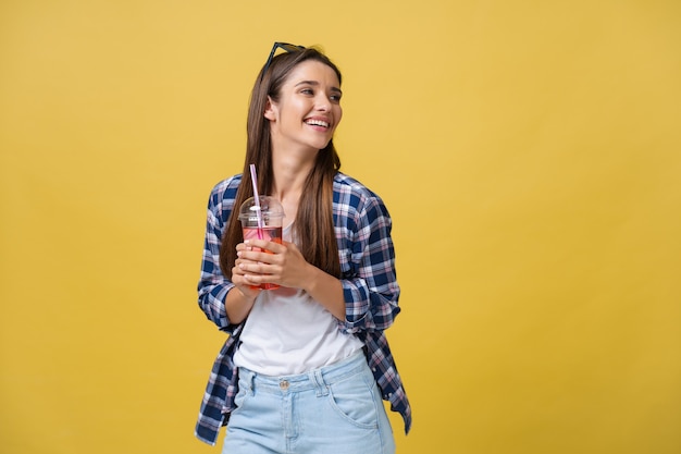 黄色の背景で隔離のトロピカルカクテルを飲むカジュアルな服を着て幸せな笑う女性。