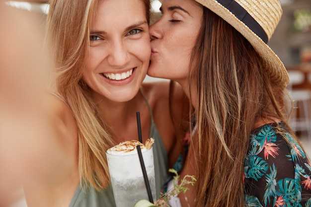 幸せなレズビアンの女性は、自分撮りを作り、情熱的にキスし、新鮮なカクテルを飲み、良好な関係と本当の愛を示します。 2人の女性観光客が夏の旅を楽しんで、一緒に夏のパーティーを持っています
