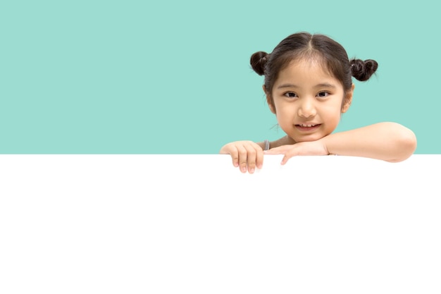 Happy little Asian child girl smiling and showing white blank sign billboard isolated on pastel green background