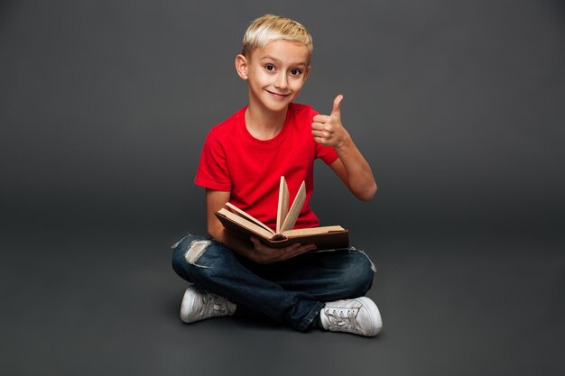 Happy little boy child reading book showing thumbs up.