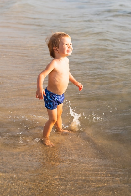 Foto gratuita ragazzino felice in riva al mare in costume da bagno