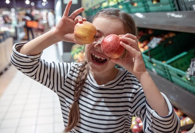 Счастливая маленькая девочка выбирает яблоки в продуктовом магазине.