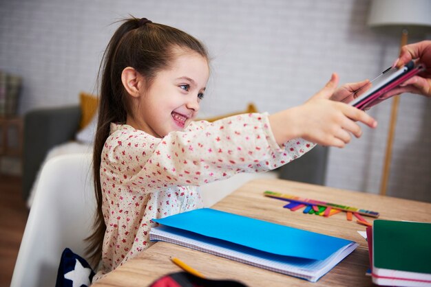 Счастливая маленькая девочка заканчивает домашнее задание и тянется к планшету