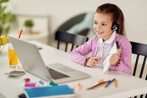 Happy little girl having online class with a teacher over laptop