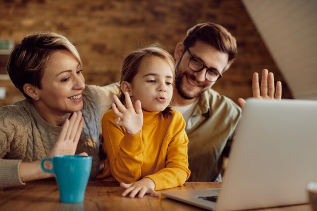 Happy little girl and her parents having video call over laptop at home
