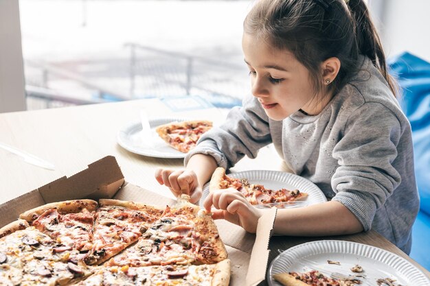 행복한 어린 소녀가 식욕으로 피자를 봅니다.