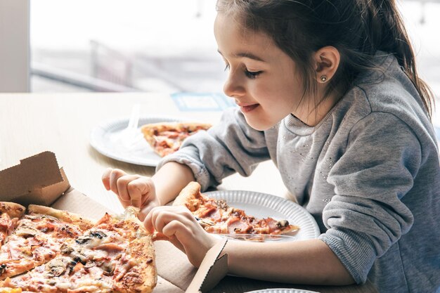 Счастливая маленькая девочка с аппетитом смотрит на пиццу