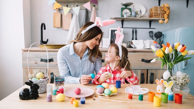 Happy little girl painting eggs for Easter with mother 