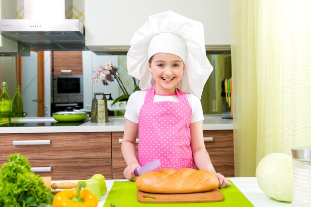 キッチンでパンを切るピンクのエプロンで幸せな少女。
